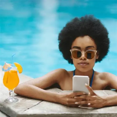 Женщина разговаривает по телефону, отдыхая в бассейне с тропическим напитком