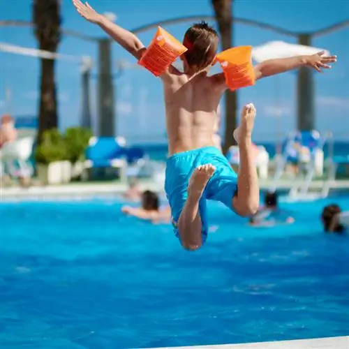 ребенок прыгает в бассейн отеля