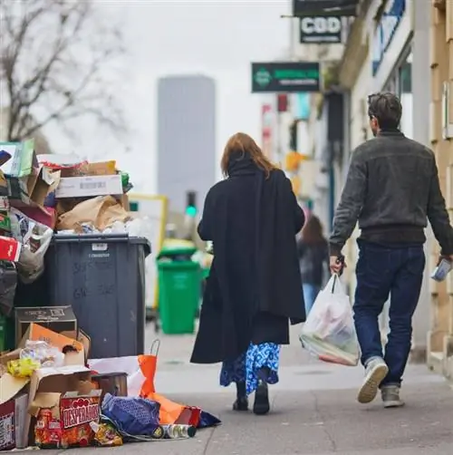 Люди идут по улице Парижа с мусором на тротуаре
