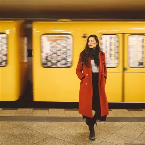 Винтажное тонированное изображение молодой брюнетки в красном пальто, стоящей на станции берлинского метро.