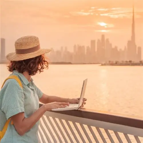 красочный закат над Дубай-Крик с женщиной за ноутбуком, вид на небоскребы и Бурдж-Халифа