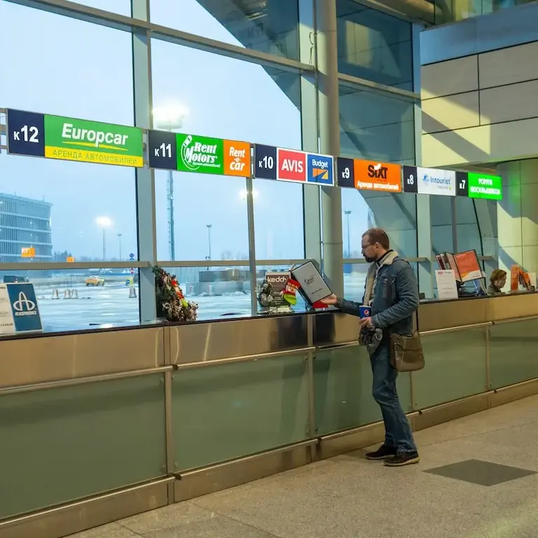 Мужчина изучает варианты аренды автомобиля на стойке аэропорта