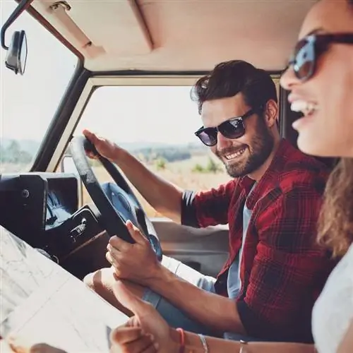 Счастливая молодая пара с картой в машине. Улыбающиеся мужчина и женщина используют карту в поездке.