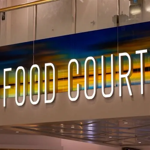 Неоновая вывеска с надписью «Фуд-корт» над коридором терминала аэропорта.