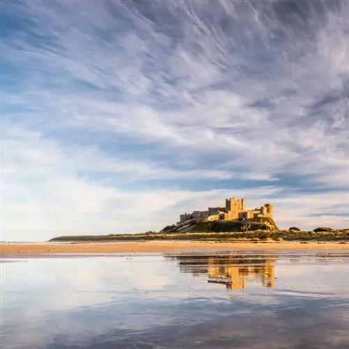 Вид на замок Бамбург, отраженный в воде пляжа внизу.