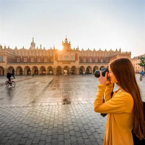 Молодая туристка с фотоаппаратом и рюкзаком фотографирует Суконные ряды в старом центре Кракова (1)