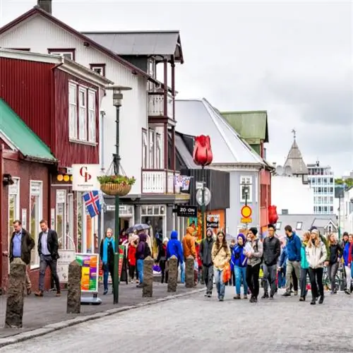 Многие туристы гуляют по тротуару в центре города возле магазинов Рейкьявика