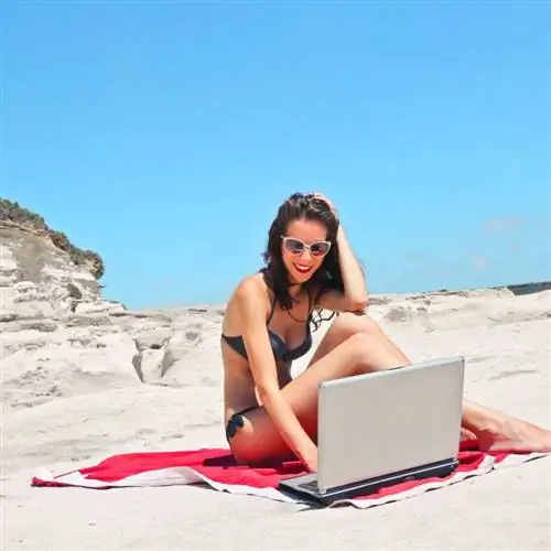 Женщина сидит на пляже и работает за ноутбуком