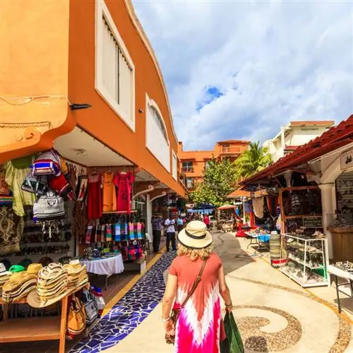 Туристка в ярком платье идет по улице с магазинами в Мексике.
