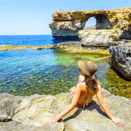 Спина женщины сидит на скале и наслаждается видом на Лазурное окно, известное туристическое направление Мальты, копию Средиземного моря