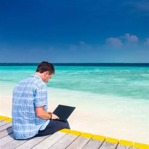 Мужчина-цифровой кочевник, работающий за своим компьютером на пляже, в Карибском море, в Средиземном или Индийском океане