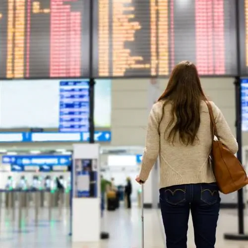 Женщина смотрит на большое табло вылета в аэропорту.