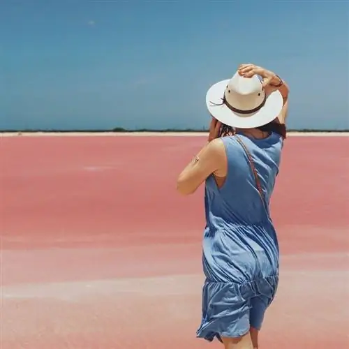Туристка в летнем синем платье и соломенной шляпе позирует для фотографии на берегу розового озера Лас-Колорадас, недалеко от Рио-Лагартос, штат Юкатан, Мексика