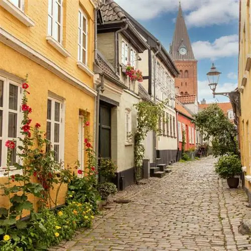 Красивая мощеная улица с желтыми домами теплых тонов и деревянной колокольней в Ольборге, Дания