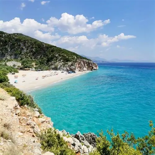 Пляж Гджипе с белым песком, туристическими палатками и зонтиками, бирюзовое Ионическое море, спрятанное между горами в каньоне в солнечный день в Албании.