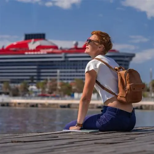 Женщина сидит перед круизным лайнером Virgin Voyages.