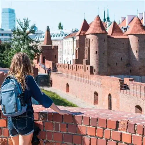 Варшава, Польша Знаменитый старый город Барбакан, историческая столица в солнечный летний день и архитектура крепости из красно-оранжевой кирпичной стены с туристическим рюкзаком для путешествий молодой женщины