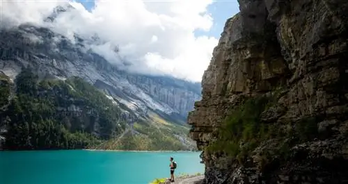 Мужчина с рюкзаком смотрит на горное озеро.