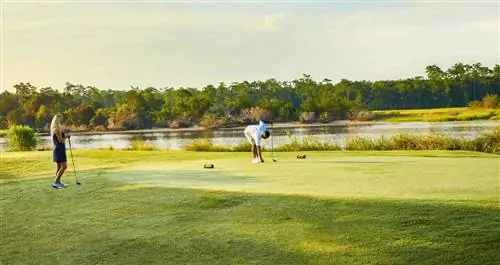 Один игрок в гольф делает удар, а другой ждет у коробки для ти.