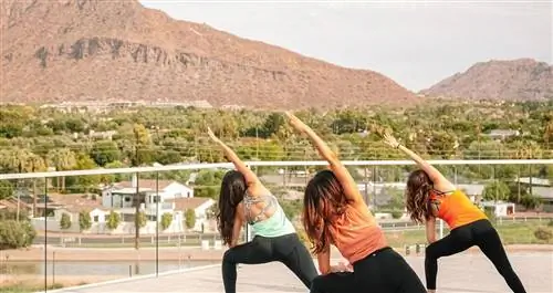Три женщины занимаются йогой на балконе с видом на пригородный район в пустыне.
