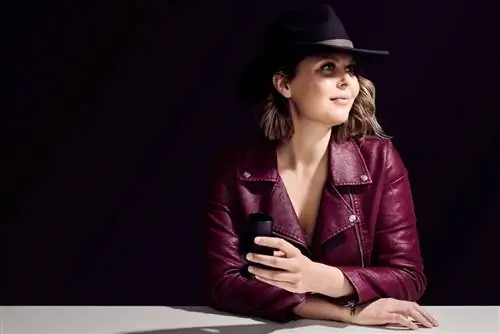 Женщина в пурпурной кожаной куртке держит темный застекленный стакан