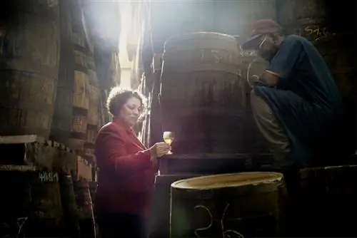 Женщина держит стакан рома в лабиринте бочек