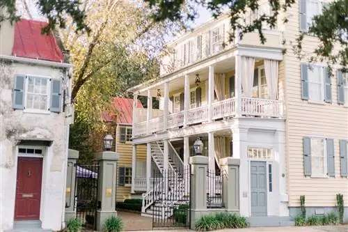 Солнце освещает кремовый многоэтажный дом с галереей и верандой перед входом.