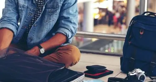 Путешественник в аэропорту с рюкзаком и открытым чемоданом