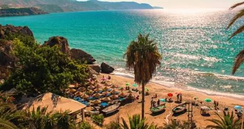 Пляж с зонтиками и пальмами на побережье Коста-дель-Соль в Испании.