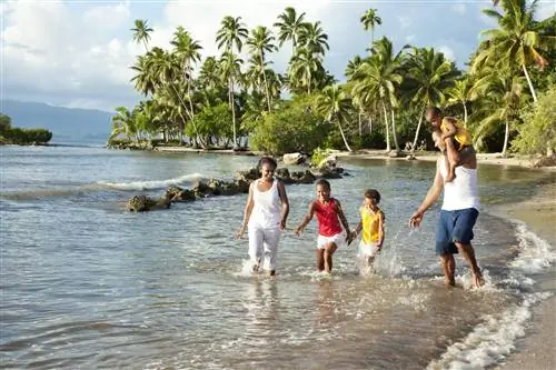 Улыбающаяся фиджийская семья из троих детей, мама и папа играют в море на белом песчаном пляже с пальмами позади них на острове Вануа-Леву на Фиджи.