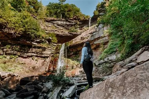 Женщина стоит на каменистой ступеньке и смотрит вверх на водопад Катерскилл.
