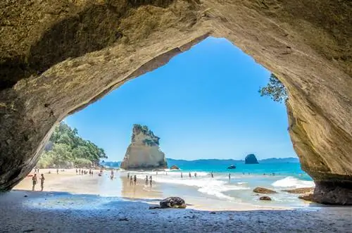 Вид через большое каменное отверстие, открывающее пляж с большим каменным сооружением в воде.