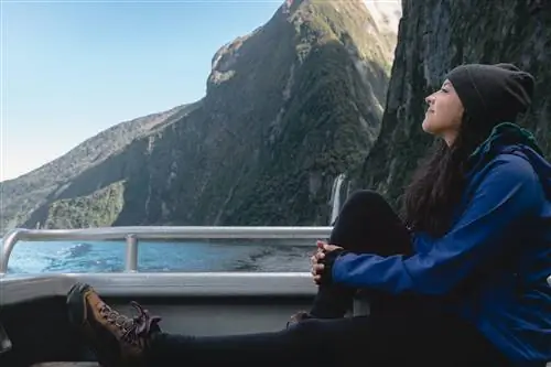 Женщина сидит на палубе лодки, глядя на окружающие ее горные пейзажи.