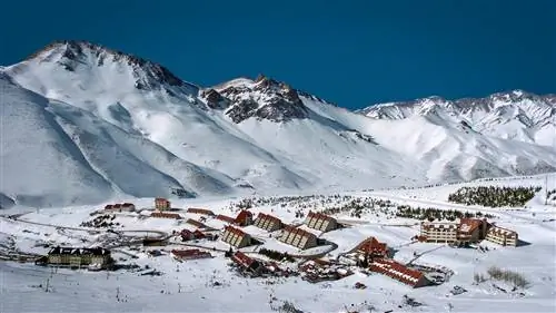 Вид на заснеженный горный хребет и треугольные домики с красными крышами в Лас-Леньяс, Аргентина.