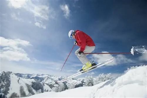 Мужчина в ярко-красной куртке и очках подышает воздухом, спускаясь на лыжах.