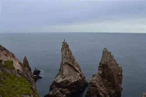 Человек стоит на вершине высокой узкой скалы, выступающей прямо из моря.