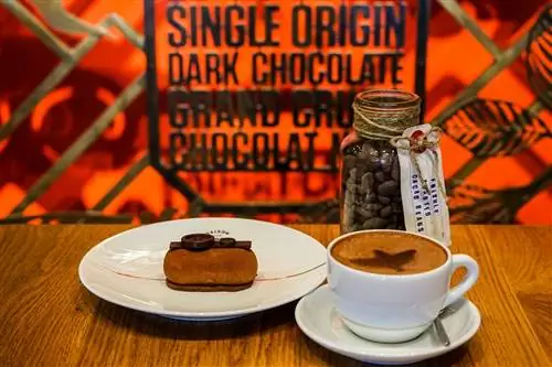 Один из красиво оформленных шоколадных десертов Maison Marou и чашка кофе на эффектном красном фоне.