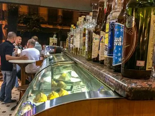 Вид сбоку продуктовой витрины с выпечкой внутри и бутылками с алкоголем наверху.