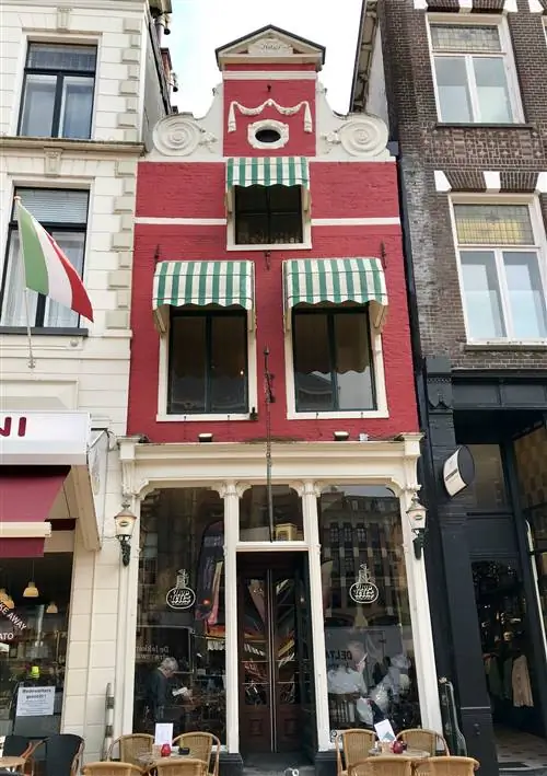 Тонкое красное здание с навесами в бело-зеленую полоску зажато между двумя другими зданиями в Гронингене, Нидерланды.