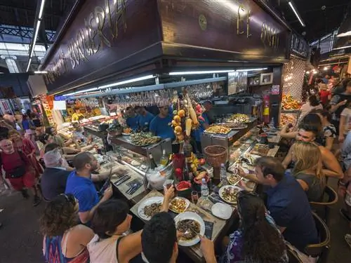 Прилавок, полный людей, которые едят тапас, в Mercat de la Boqueria, Барселона.