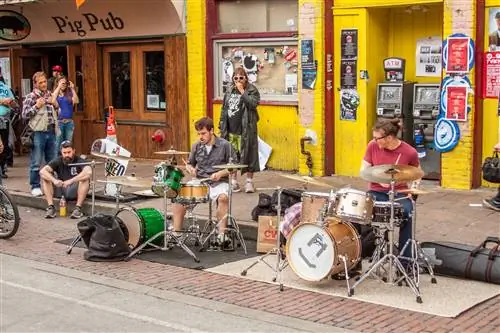 Два барабанщика играют на ударных установках на улице, а несколько человек смотрят на них.