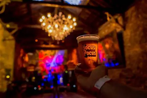 Мужчина держит чашку пива со словами «Фокус-покус» в атмосферном музыкальном зале с большой люстрой в Рио-де-Жанейро, Бразилия.