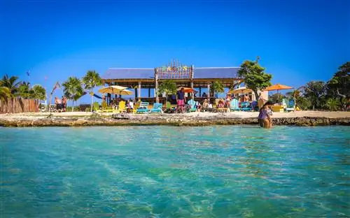 Несколько человек слоняются по воде и возле пляжного бара.