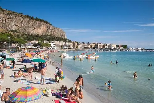 Многие люди отдыхают на песчаном пляже или играют в спокойном море в солнечный день.