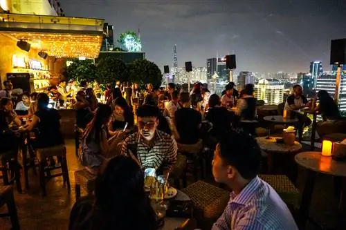 Гуляки собираются в баре на крыше Saigon Social Club, чтобы выпить и поужинать. Пространство мерцает свечами и гирляндами, а также городскими огнями на заднем плане.