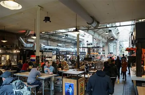 Интерьер Foodhallen в Амстердаме с людьми, которые едят за общими столами. Интерьер Foodhallen в Амстердаме с людьми, которые едят за общими столами.