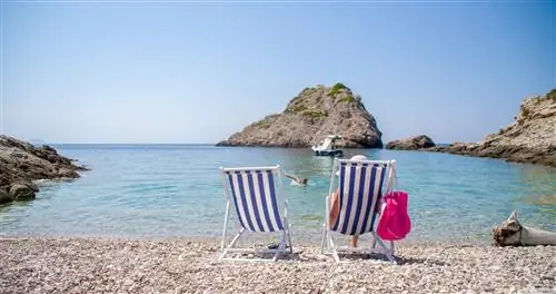 Два человека сидят в бело-голубых шезлонгах на идиллическом пляже в Хорватии.