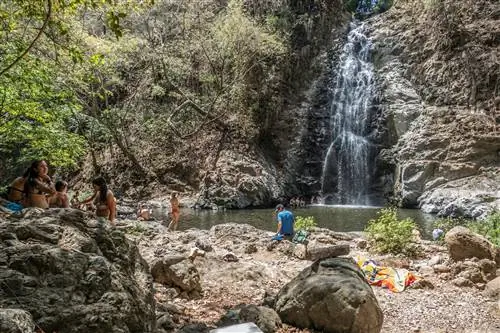 Небольшие группы людей в купальных костюмах собрались на скалистой земле вокруг водопада Монтесума в Коста-Рике.