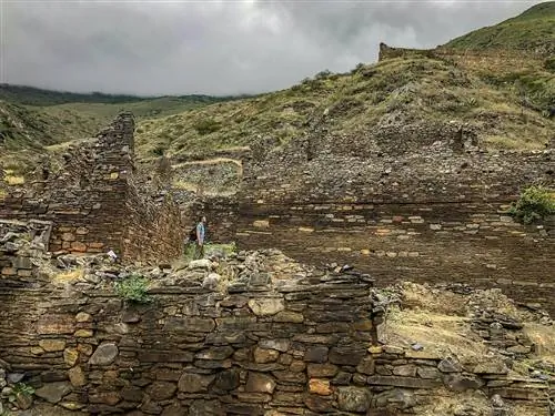 Мужчина стоит среди разрушенных каменных стен в пасмурный день в Исканвайе, Боливия.