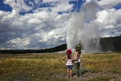 Две молодые девушки смотрят, как Old Faithful извергается в пасмурный день.